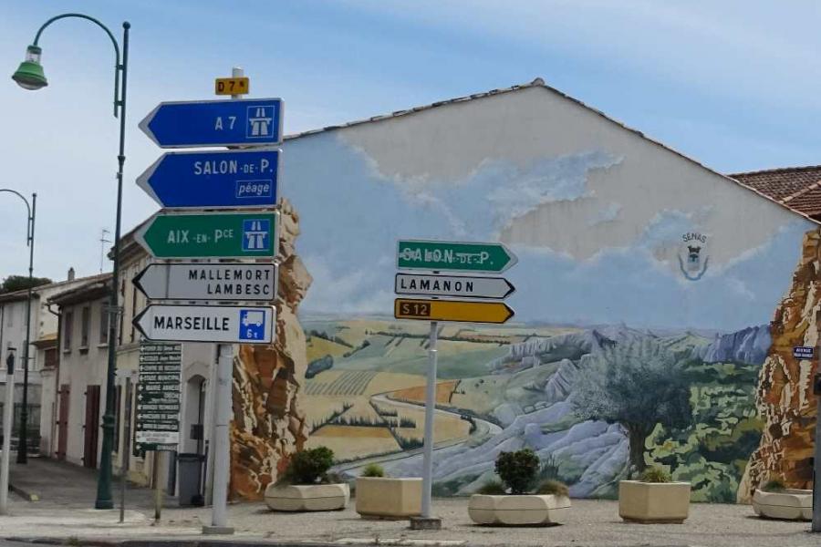 a painting of mountainpasses on a buidling, with signs to show us the way.