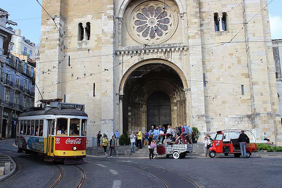 Lisbon Tram 28 and tuk tuks in front of a cathedral