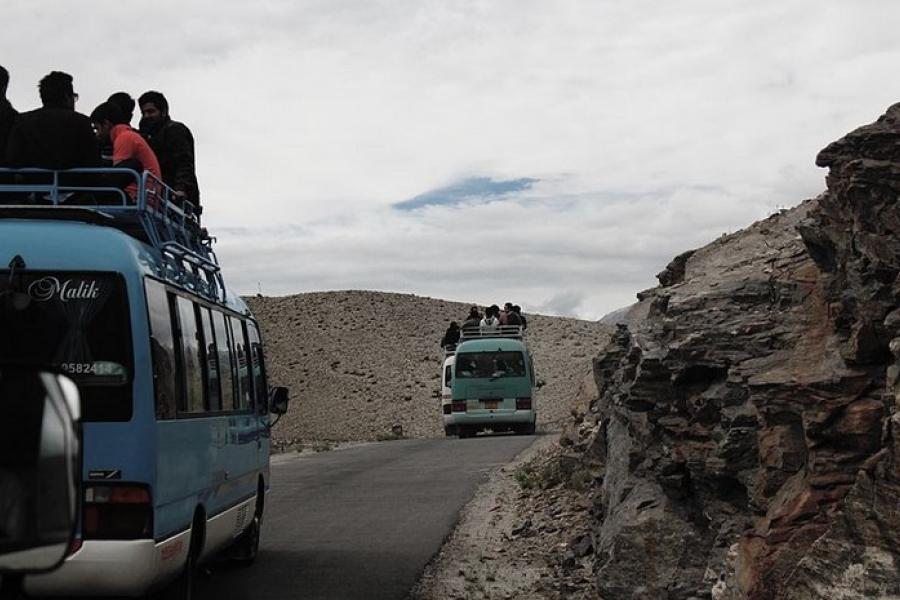 Karakoram Highway - Busses carrying passengers to Gilgit City. Some passengers are seated on top of the busses. The surrounding land is dry, dusty, and rocky.