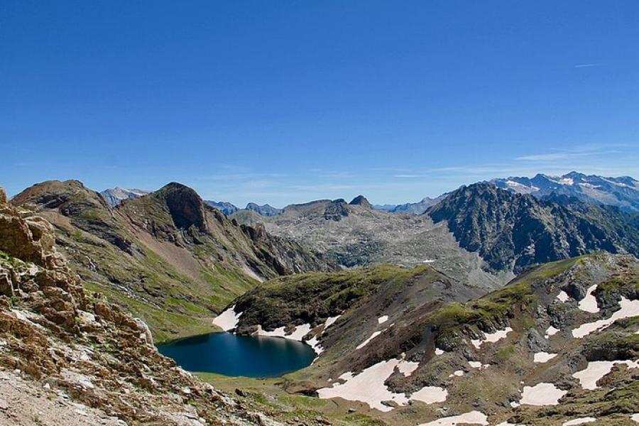 Pyrenees - High-altitude azure lake in the mountains. Some snow dotting the area, but otherwise some green and very rocky.