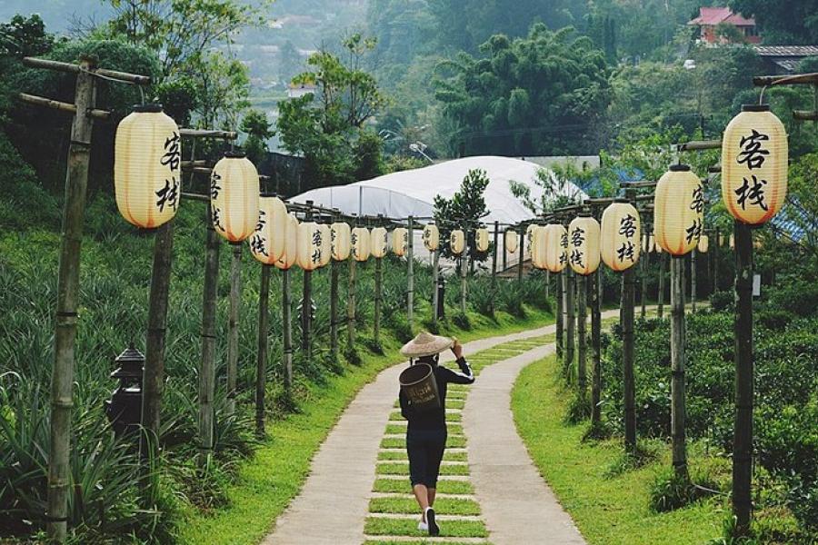 Mae Hong Son Loop, Thailand - A woman wearing a peaked sunhat walks away from the camera along a tiled walkway lined on both side with large paper lanterns on poles. Asian script is painted in black in on the lanterns.