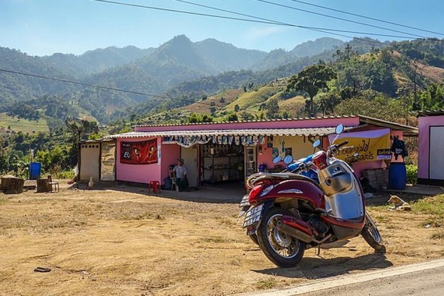 Mae Hong Son Loop, Thailand - A shiny Vespa-type moped parked by a roadside market on a sunny day.